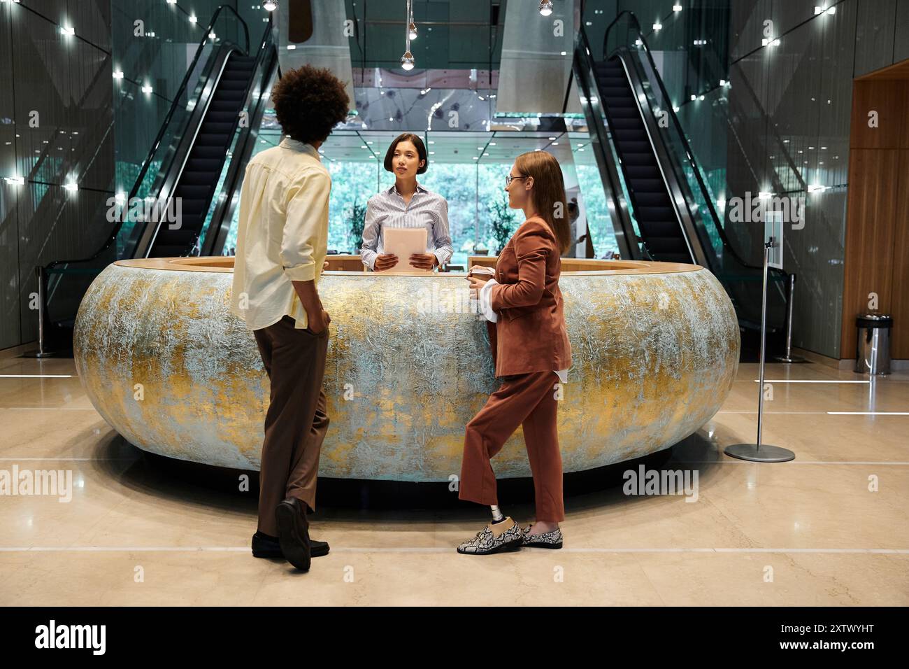 A diverse group of colleagues chat in the office lobby, sharing a friendly conversation while standing by a unique counter. Stock Photo