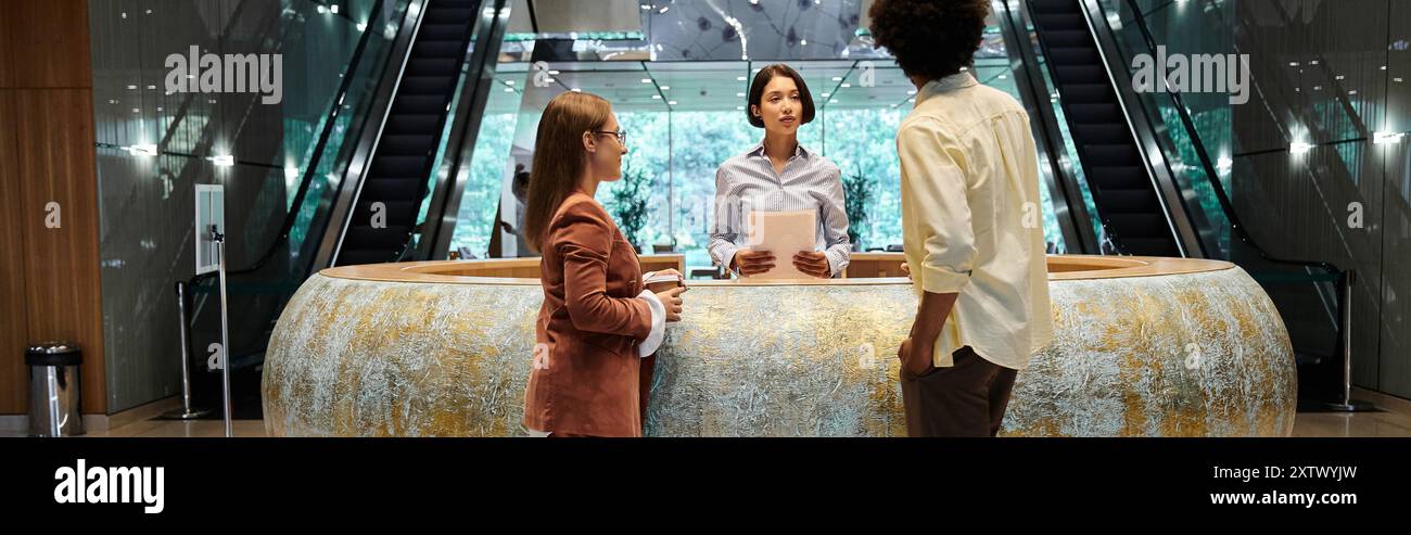 Three colleagues chat in an office lobby, with an escalator in the background, showcasing diversity. Stock Photo