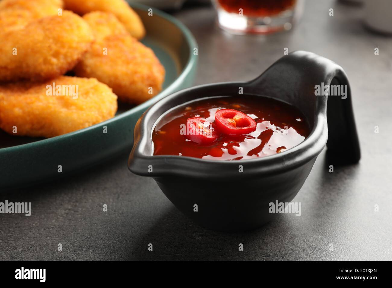 Hot chili sauce in gravy boat on grey textured table, closeup Stock Photo