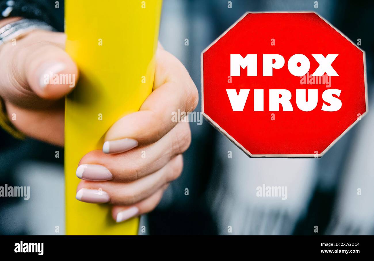 A hand holds a yellow pole while a red warning sign about mpox virus is ...