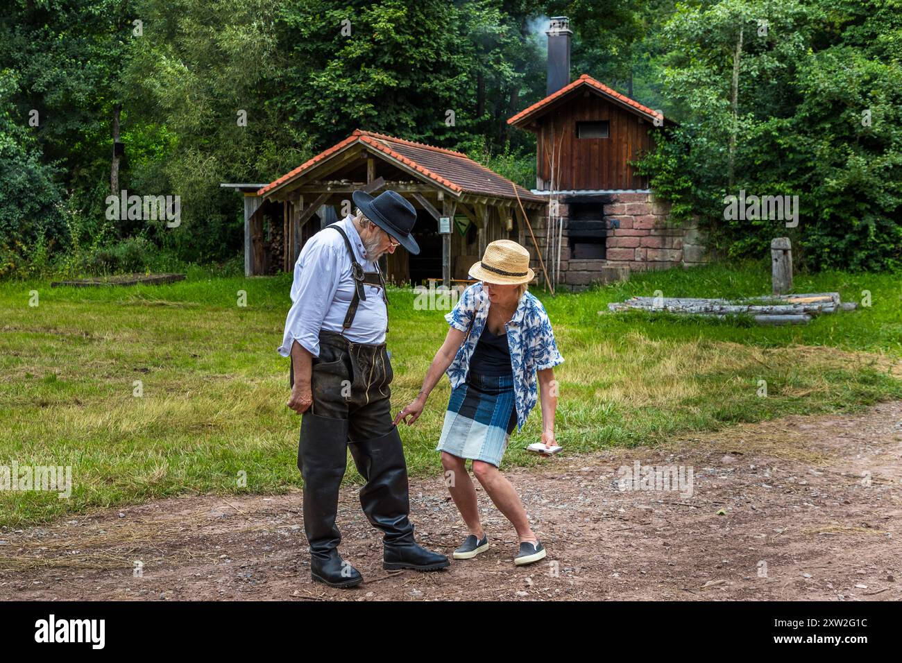 Raftsman Martin Spreng walks with journalist Angela Berg across the forecourt of the Monhardter Wasserstube near Altensteig, Baden-Württemberg, Germany. Both look down at a device in her hand. Spreng, chairman of the German Rafting Association, demonstrates historical Black Forest rafting at the site. Rafting has been recognised as UNESCO intangible cultural heritage since 2022. Stock Photo