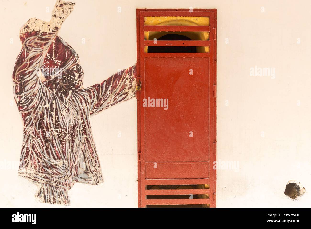 Mural of a figure appearing to open a dark rust-colored iron door in a light-colored wall. Stock Photo