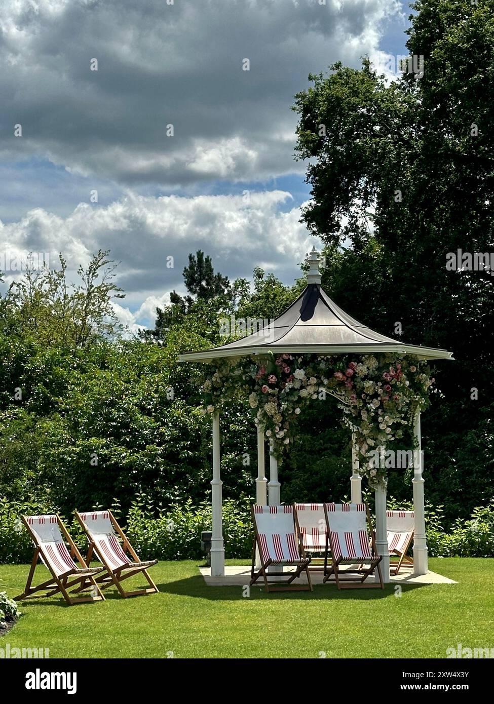 A picturesque garden gazebo adorned with flowers and surrounded by deck chairs in Egham, England Stock Photo