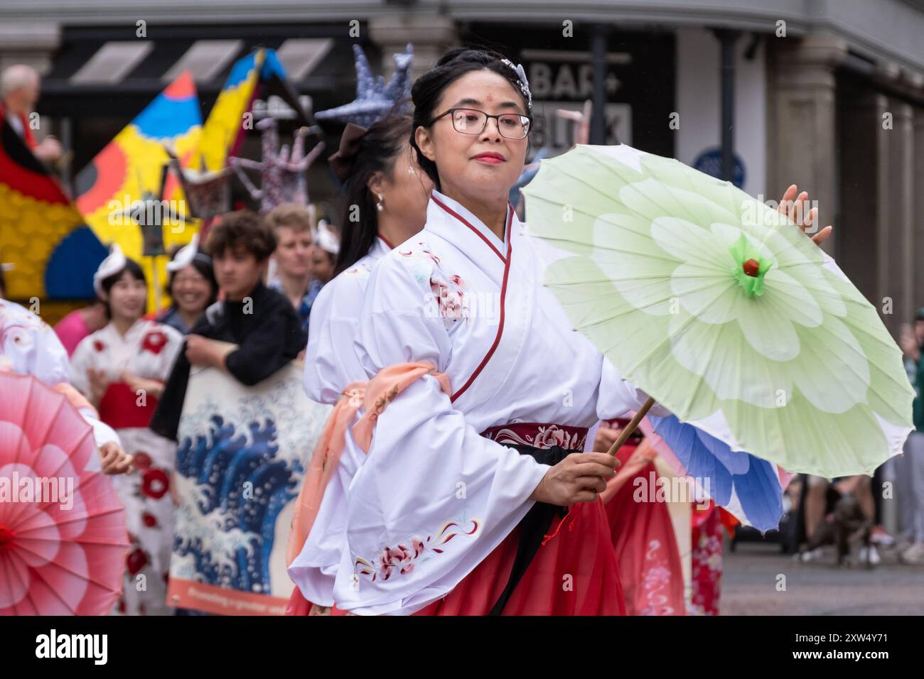 Belfast Mela Carnival Parade - elegant lady in traditional Japanese costume with green parasol moves with great poise. Belfast, UK - Aug 17, 2024. Stock Photo