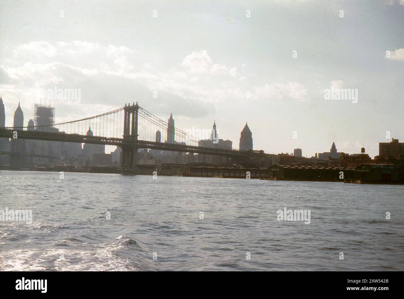 New York, USA. September 1959 – A view of Manhattan Bridge from the East River. Beyond is Brooklyn Bridge and the New York skyline, silhouetted against the sky.  Visible in the foreground are Piers 33-38. The photograph also shows the One Chase Manhattan Plaza building under construction. Stock Photo