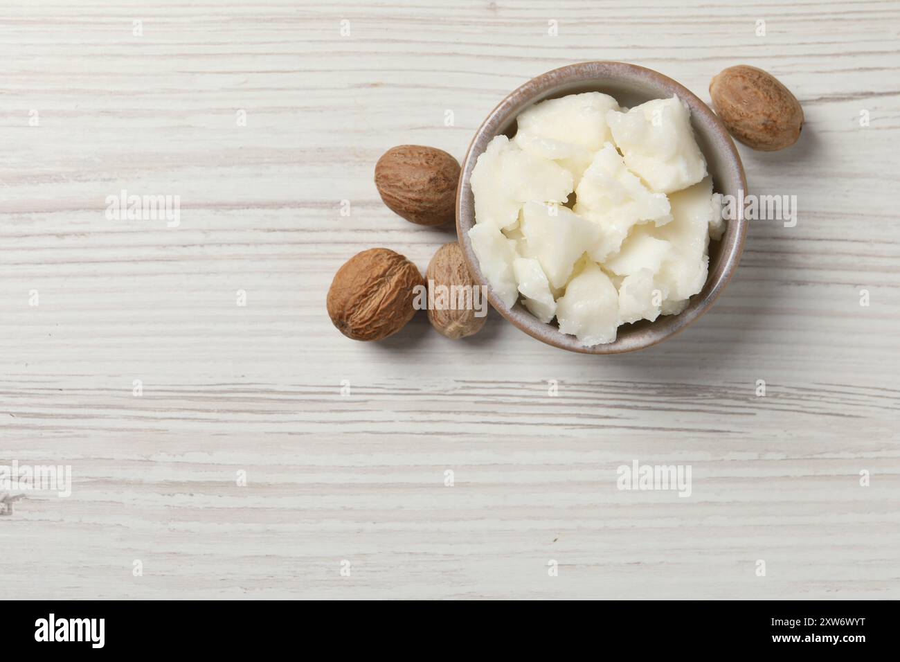 Shea butter in bowl and nuts on white wooden table, top view. Space for ...