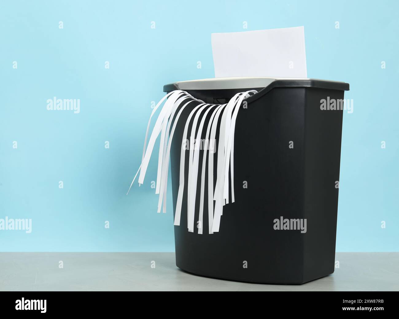 Destroying sheet of paper with shredder at grey table against light ...