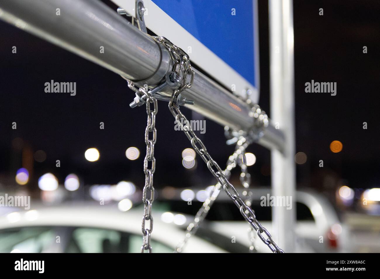 Close-up of a silver chain and padlock securing a blue sign to a metal pole - with blurred vehicles. Taken in Toronto, Canada. - Stock Image