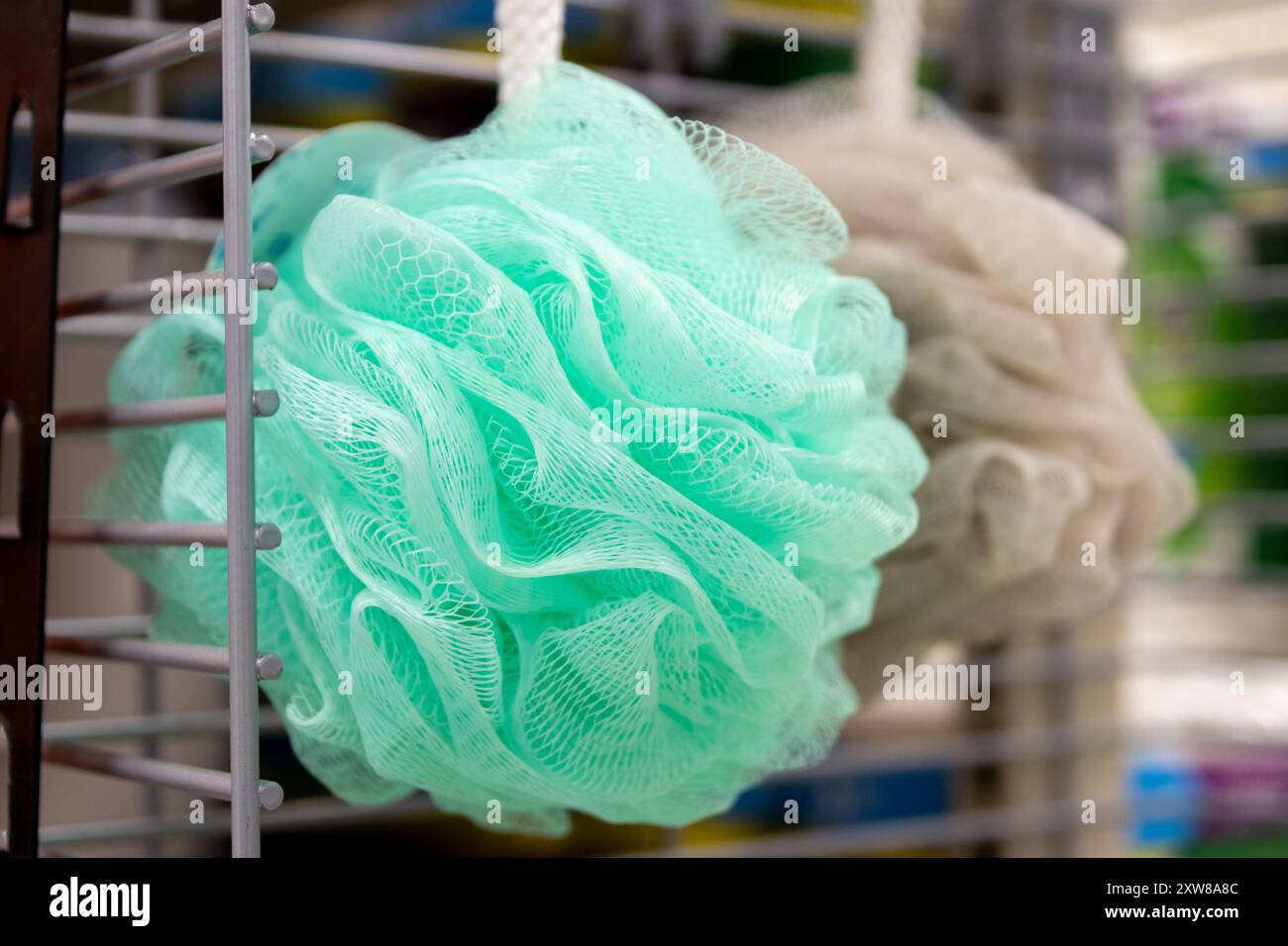 Vibrant mint green and neutral beige bath loofahs hanging on a metal store display - close-up shot. Taken in Toronto, Canada. - Stock Image