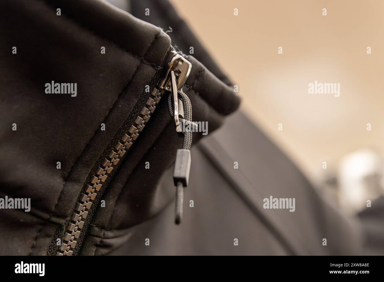 Close-up of a zipper on black fabric, highlighting the metal teeth and pull tab. Taken in Toronto, Canada. - Stock Image