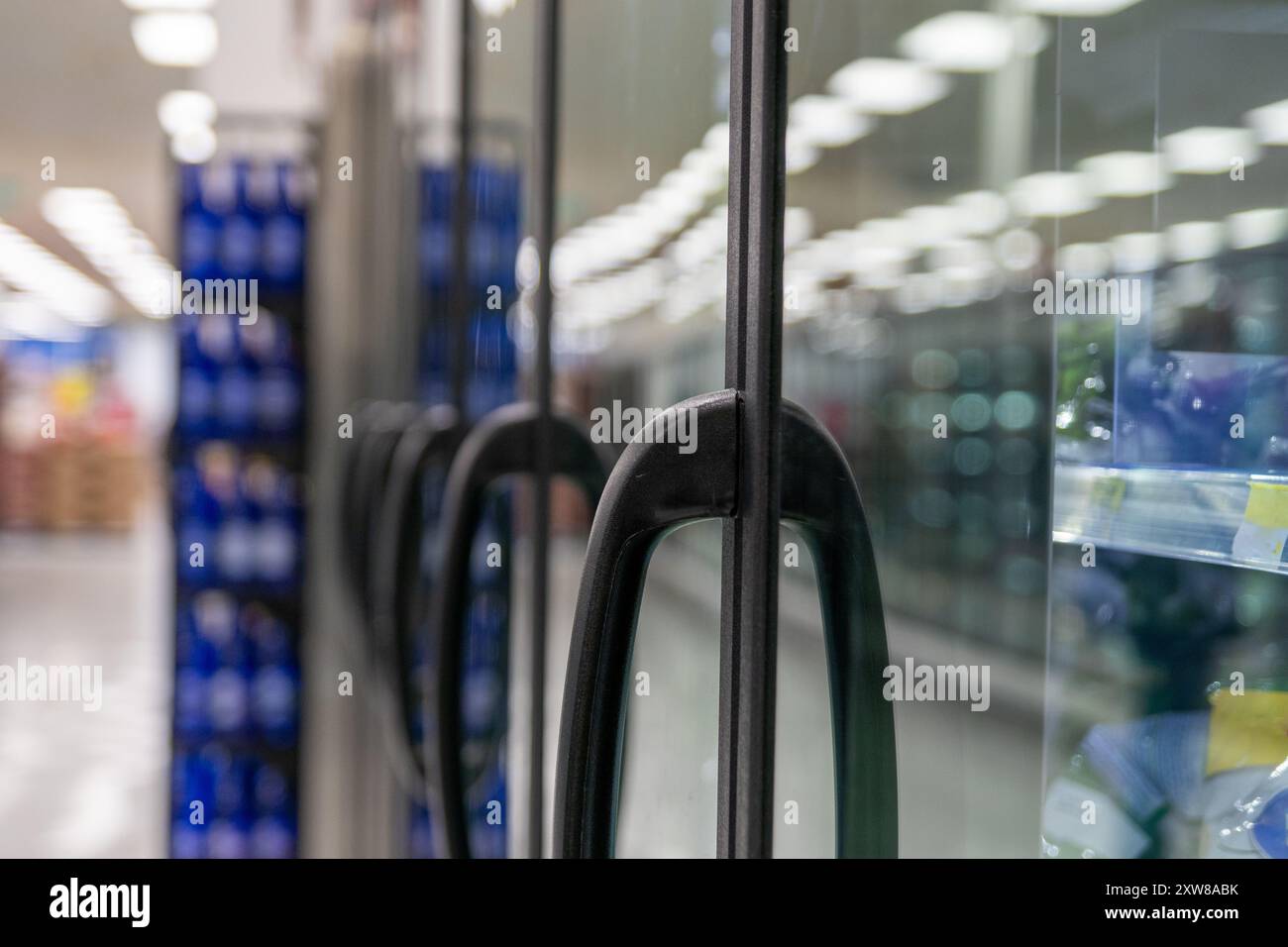 Sleek black handle of a refrigerator door in a grocery store - products blurred in the background. Taken in Toronto, Canada. - Stock Image