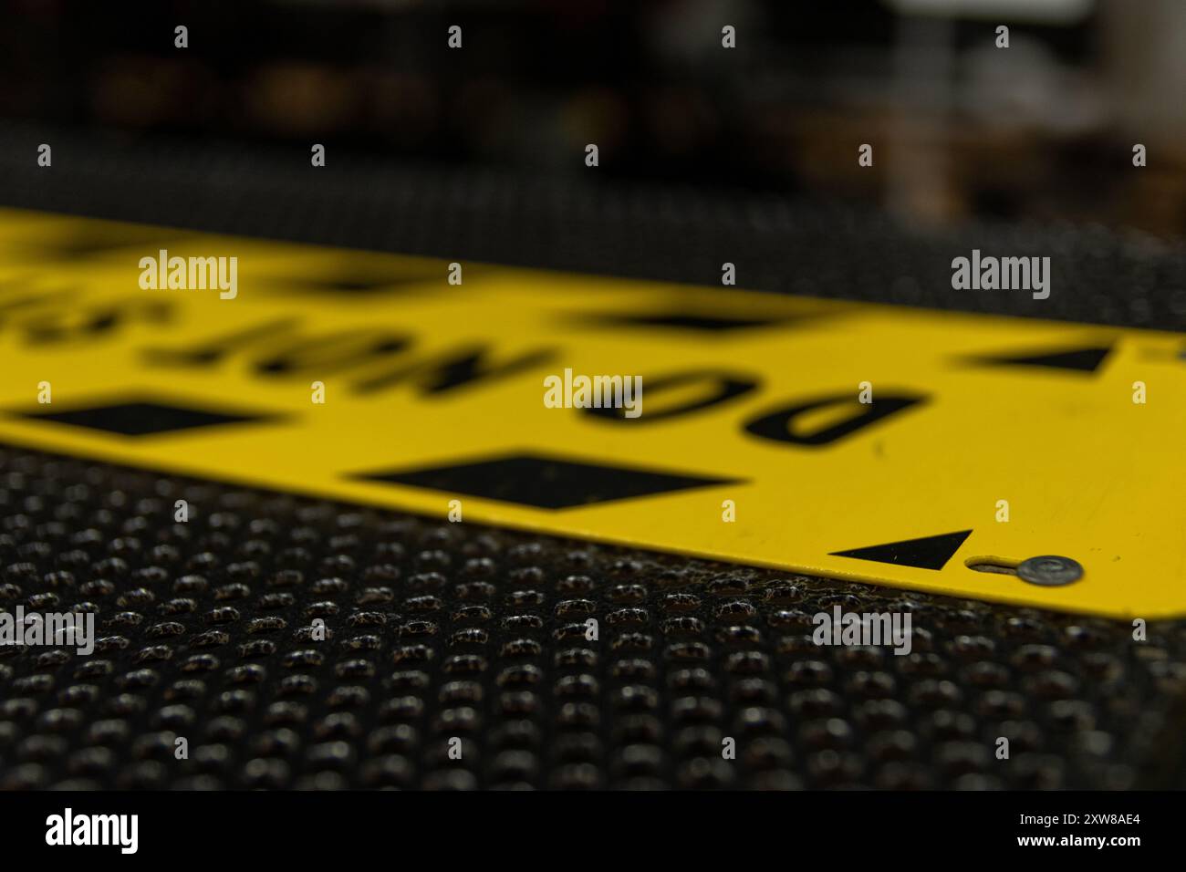 Bright yellow caution sign with bold black lettering and triangular symbols lying on a textured black surface. Taken in Toronto, Canada. - Stock Image