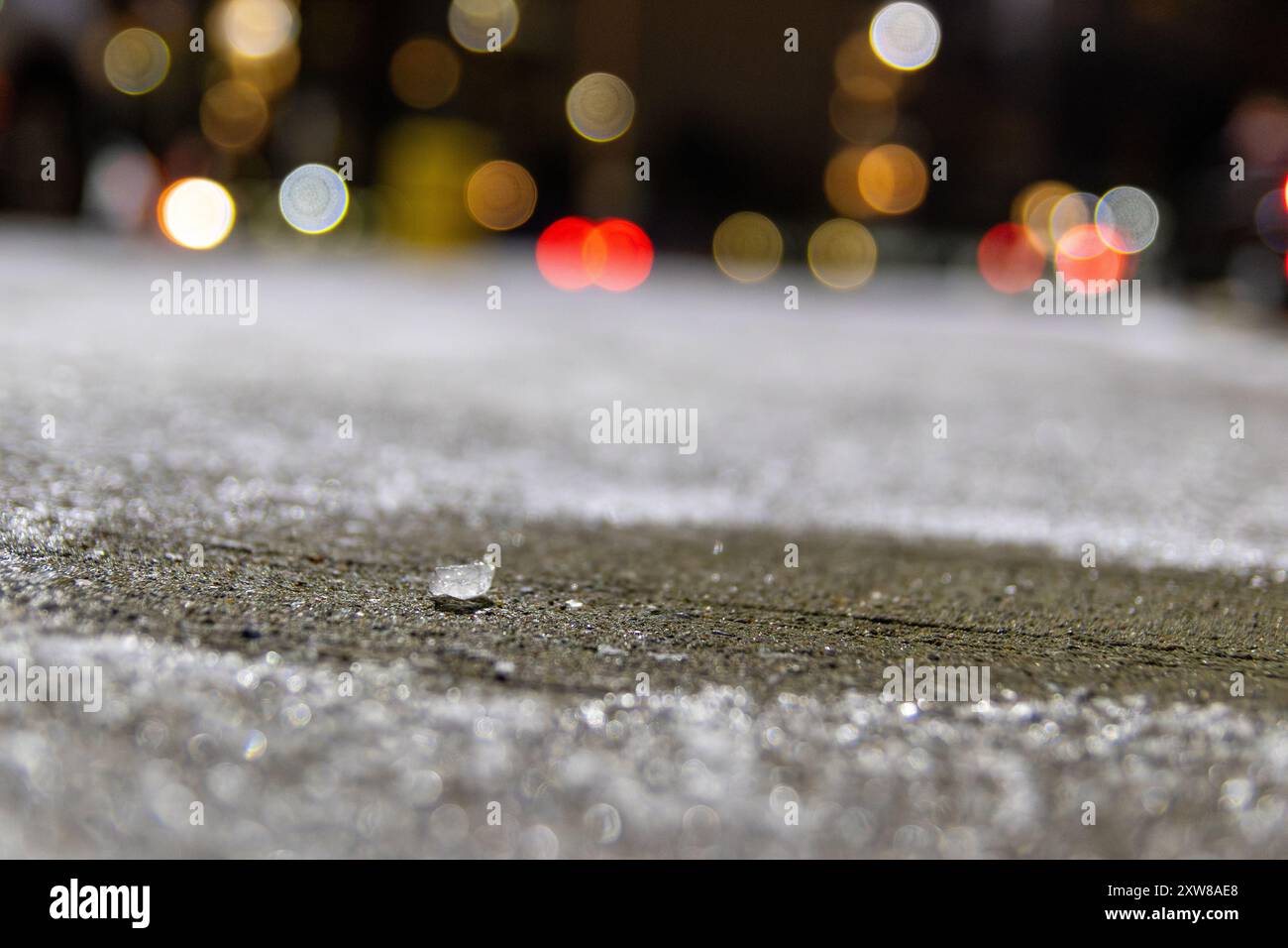 Close-up of a single road salt crystal on gritty asphalt with blurred city lights in the background. Taken in Toronto, Canada. - Stock Image