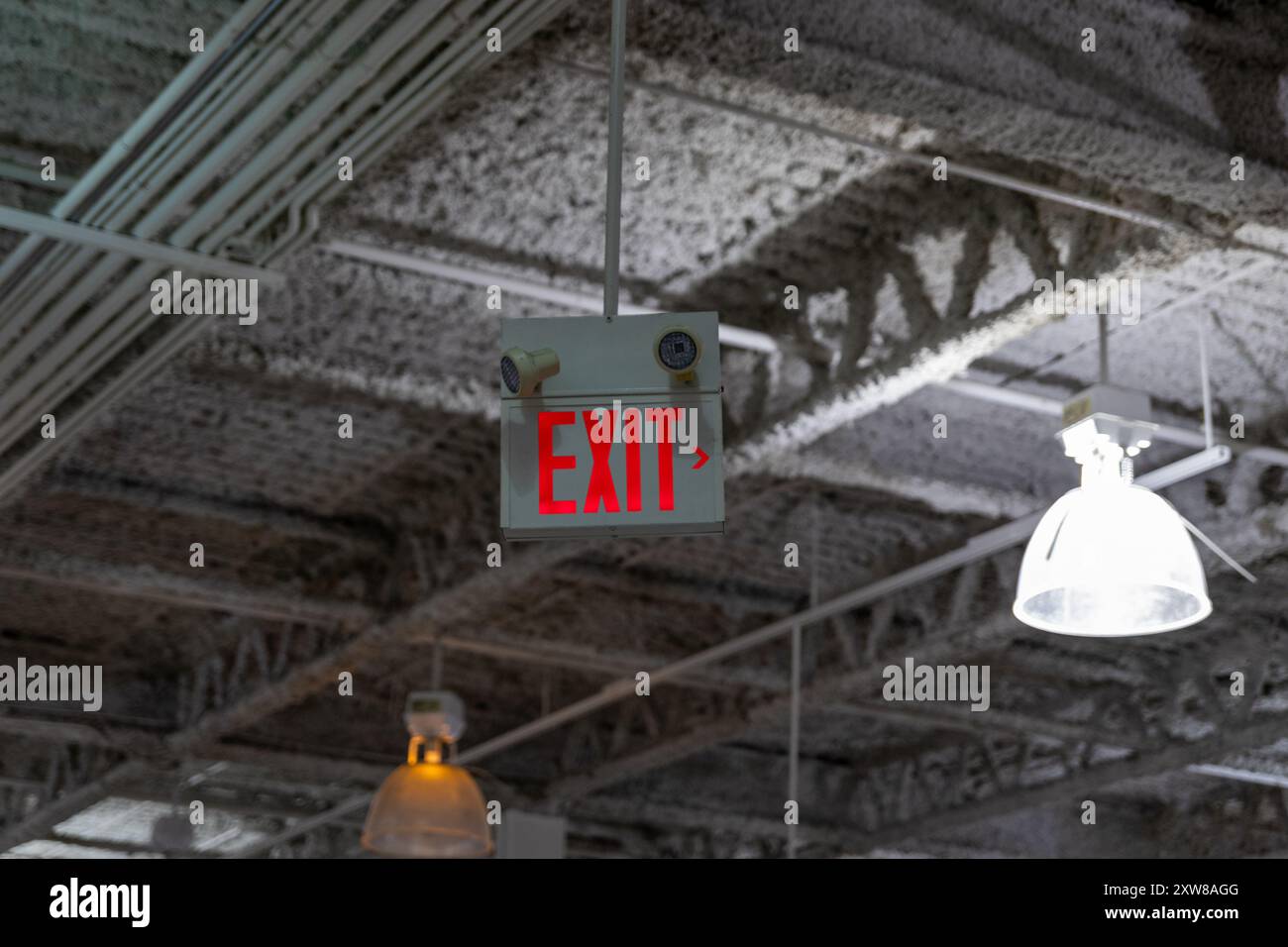 Exit sign with white lettering and right arrow - hanging from industrial ceiling. Taken in Toronto, Canada. - Stock Image