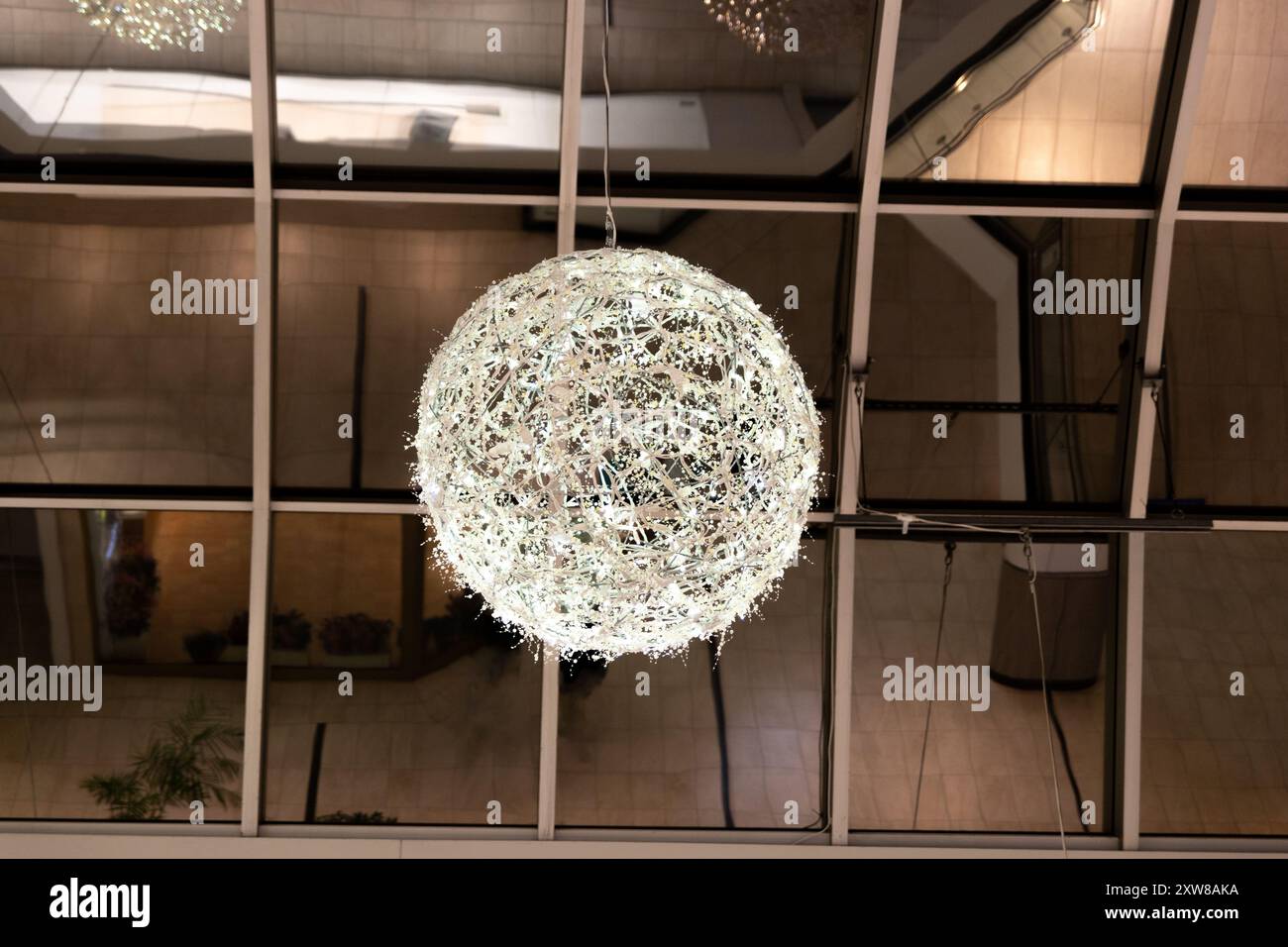 Suspended intricate white light sphere casts a soft glow in a modern interior space. Taken in Toronto, Canada. - Stock Image