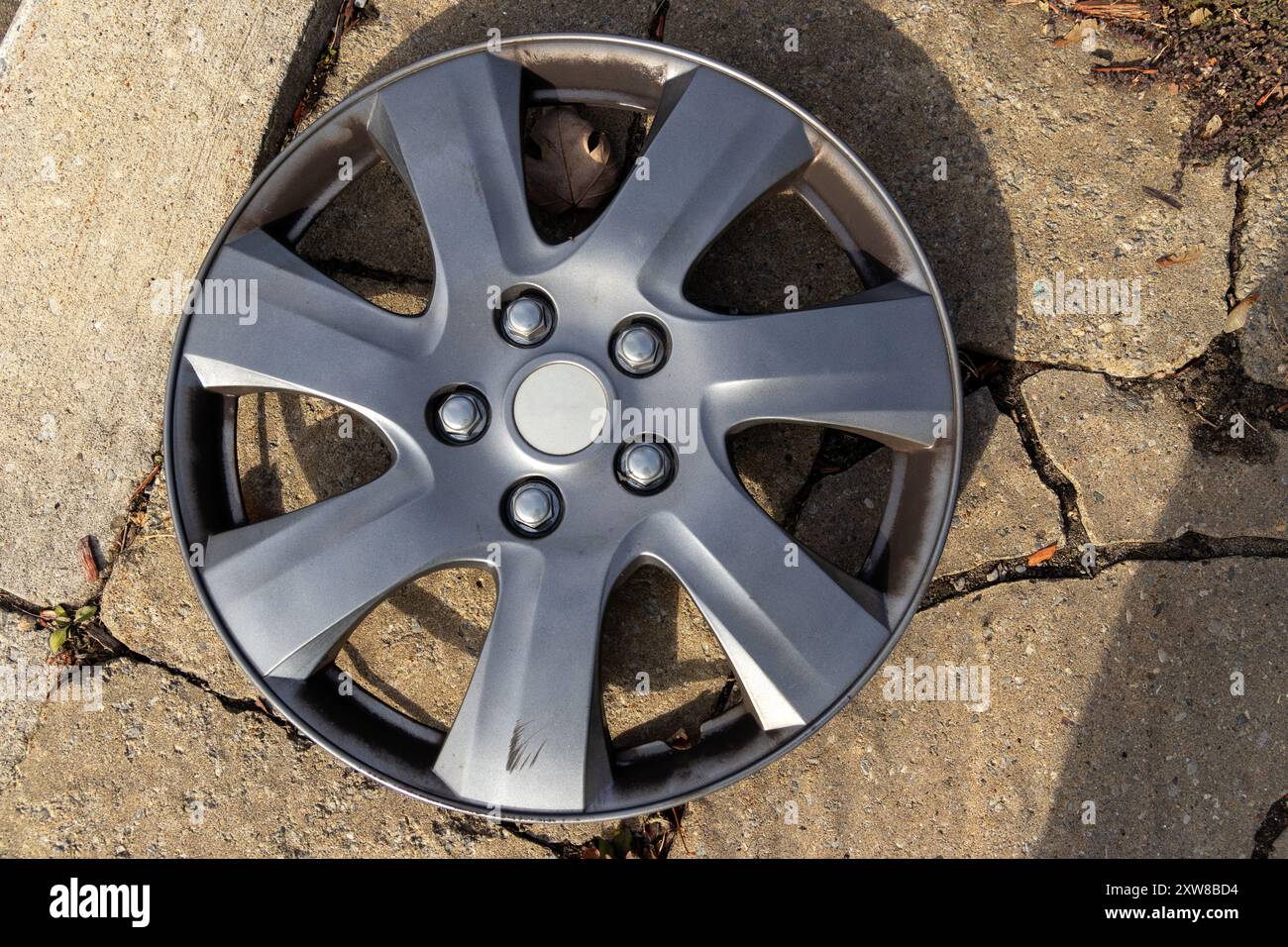 Silver car wheel hubcap resting on concrete ground - sunlight casting shadows. Taken in Toronto, Canada. - Stock Image