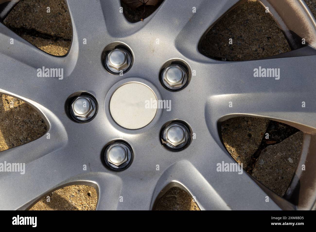 Close-up of a silver car wheel hub - showcasing lug nuts and alloy spokes against a gritty asphalt background. Taken in Toronto, Canada. - Stock Image