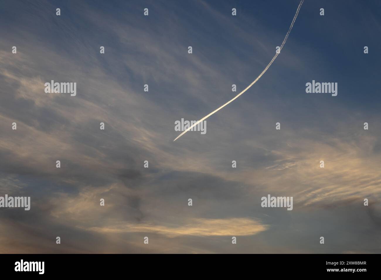 Sunset sky painted with wispy cirrus clouds and a striking contrail from an airplane cutting through. Taken in Toronto, Canada. - Stock Image