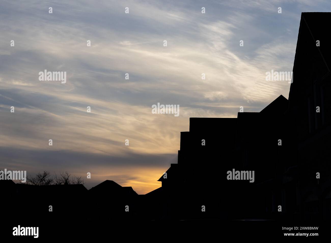 Sunset silhouette of suburban houses against a dramatic sky - wispy cirrus clouds streak above as the day fades into twilight. Taken in Toronto, Canad - Stock Image