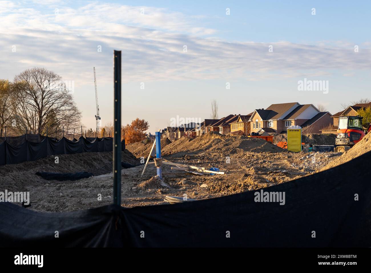 Golden hour at a suburban construction site - earth mounds and building materials foreground. Taken in Toronto, Canada. - Stock Image