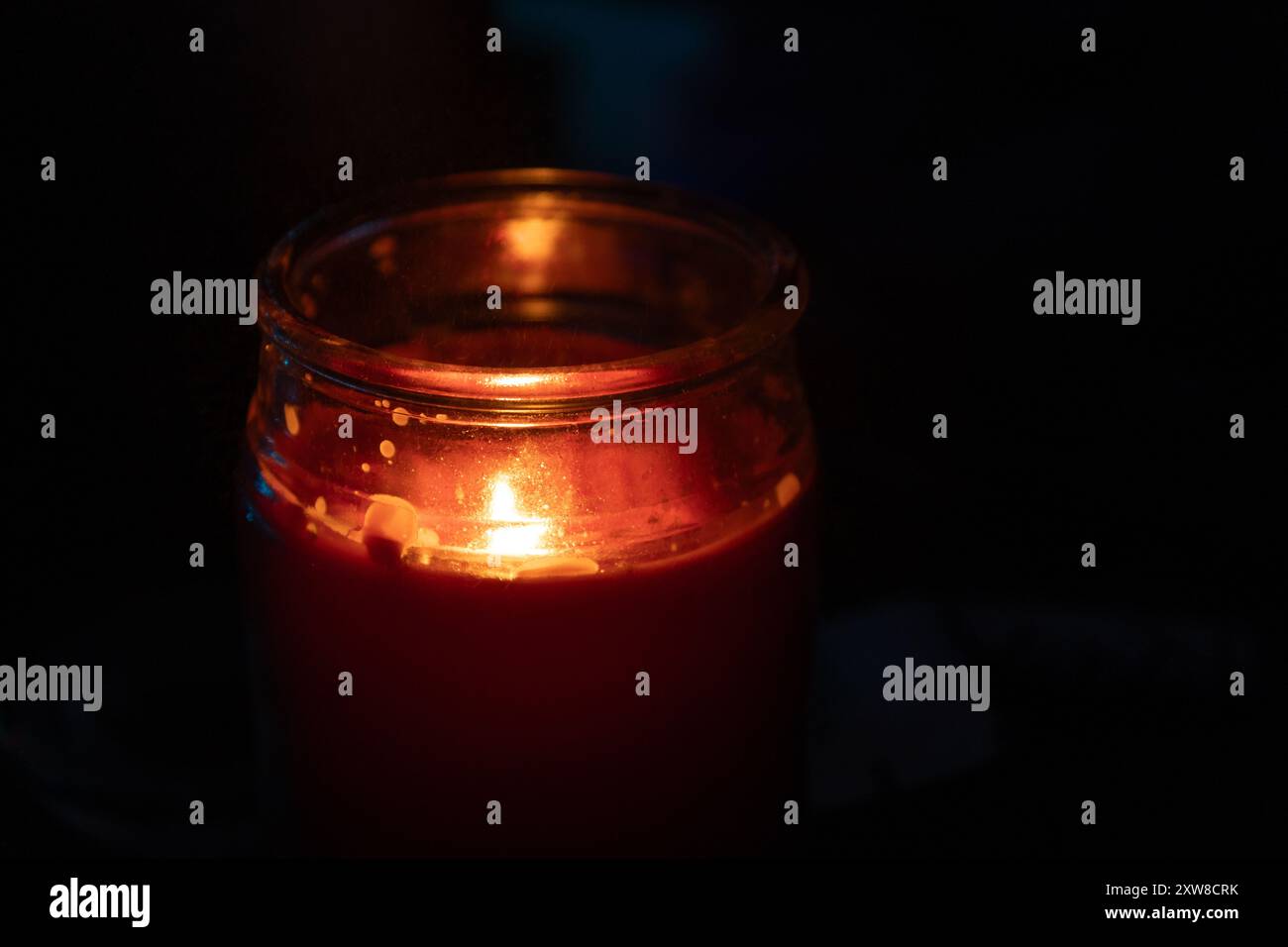 Glowing red candle in a glass jar - warm light illuminating the dark surroundings - focus on the single flickering flame. Taken in Toronto, Canada. - Stock Image