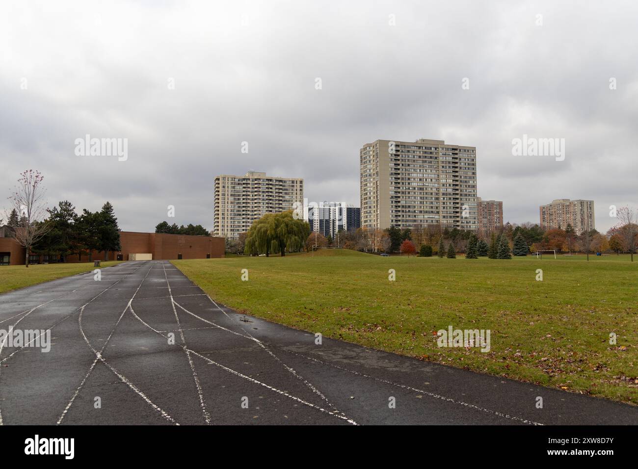 Overcast sky looms over a sprawling urban park with a running track, flanked by high-rise apartment buildings. Taken in Toronto, Canada. - Stock Image