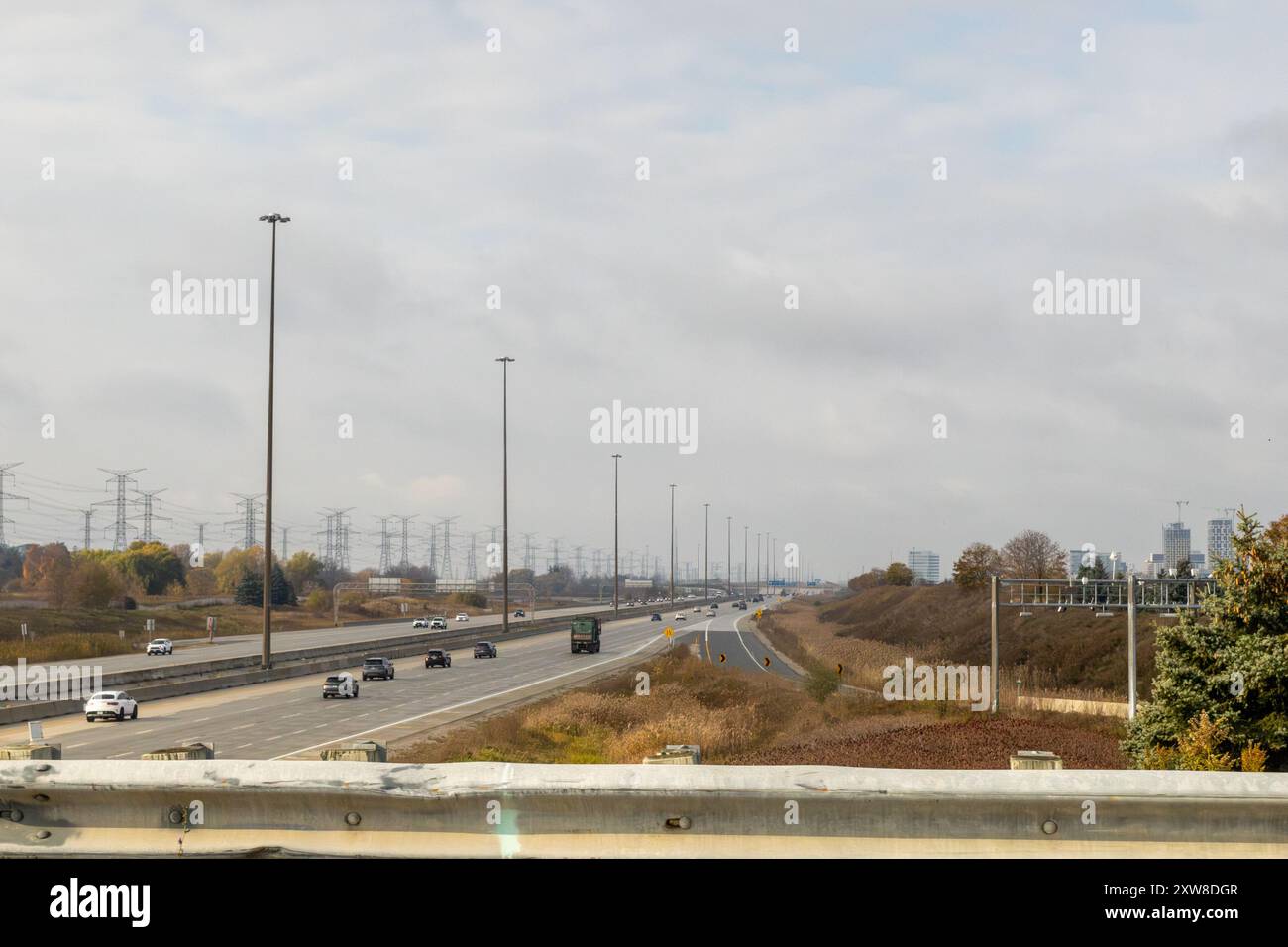 Overcast sky above a bustling highway, flanked by power lines and buildings - vehicles in motion. Taken in Toronto, Canada. - Stock Image