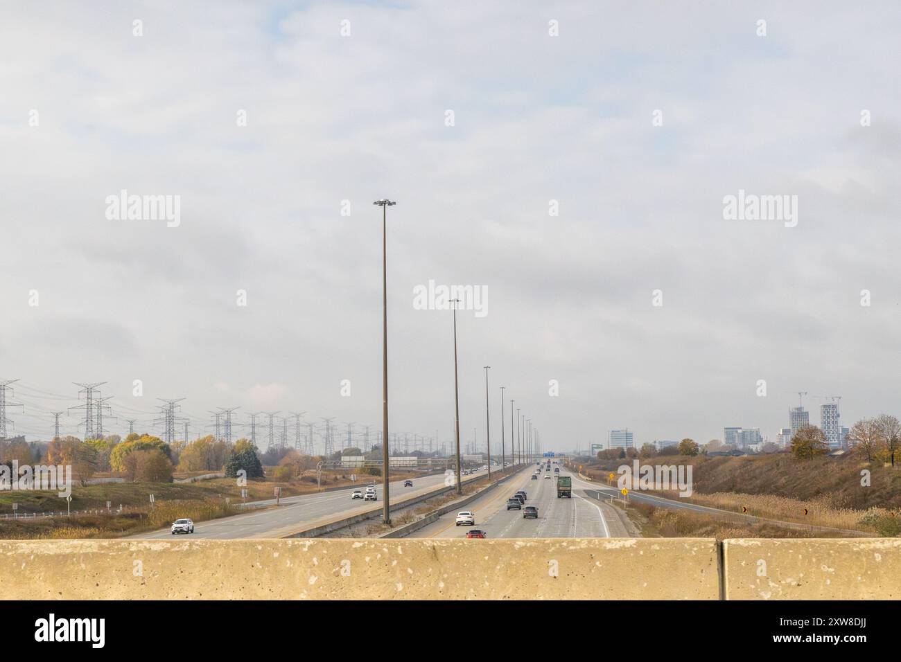 Overcast sky above a bustling highway, flanked by power lines and buildings - vehicles in motion. Taken in Toronto, Canada. - Stock Image