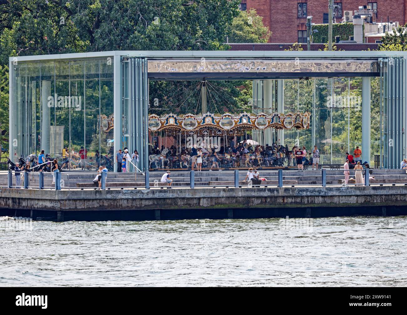 Jane’s Carousel stands in the shadow of the Brooklyn Bridge. The glass-enclosed amusement was moved from Youngstown, Ohio. View from East River ferry. Stock Photo