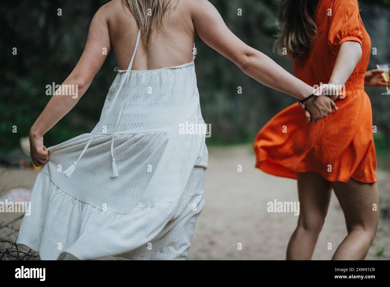 Two women holding hands and dancing outdoors in casual summer dresses ...