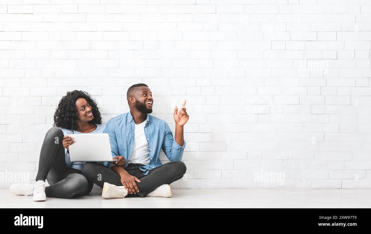 Young couple with laptop pointing at empty space Stock Photo
