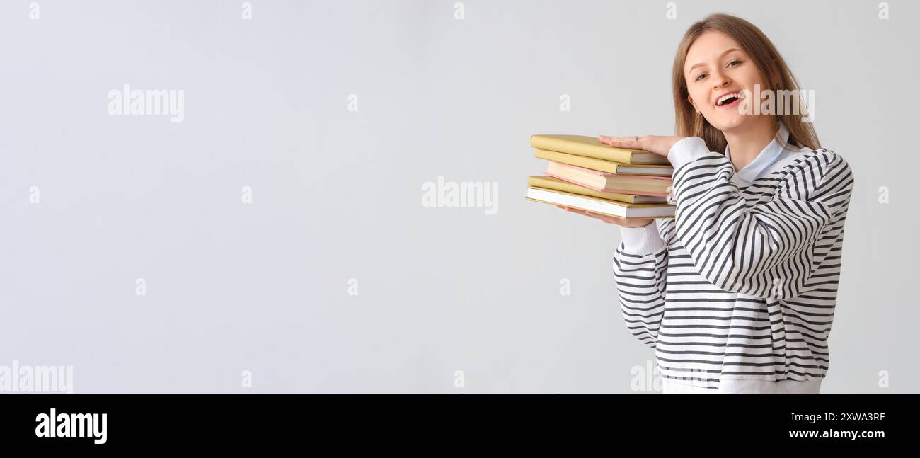 Happy female student holding stack of books on light background with ...