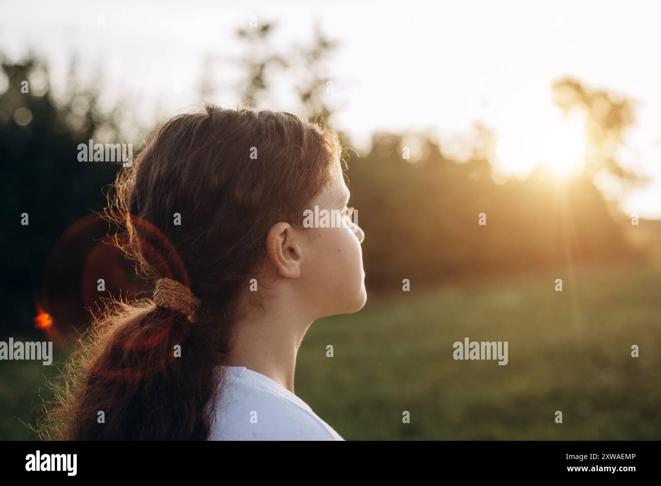 Side view of happy beautiful preteen girl standing on meadow near green ...