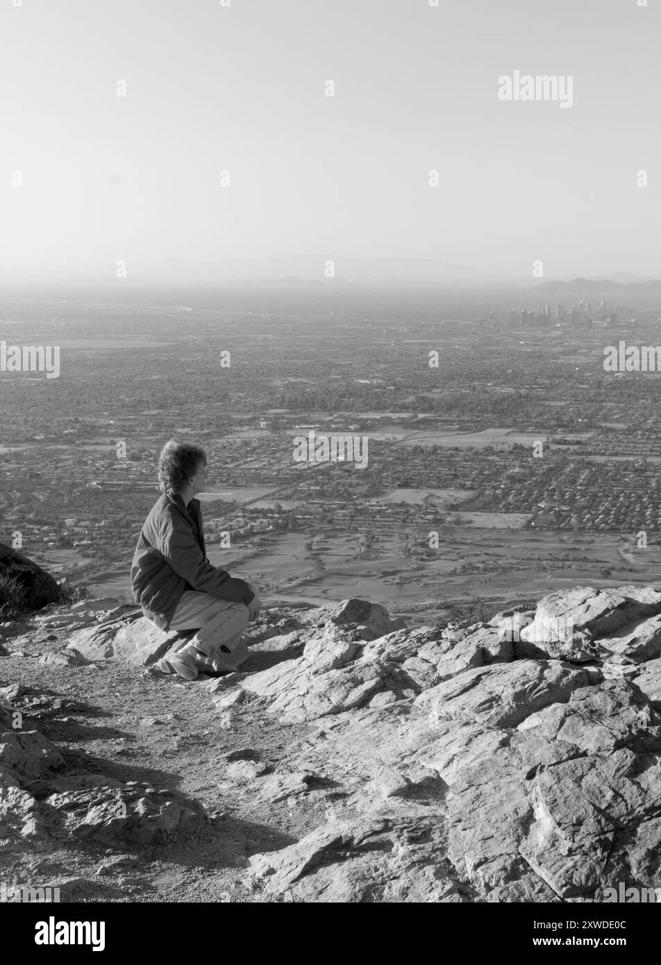 A Caucasian woman aged 50-60 sits on a rock at Dobbins Lookout, South Mountain Park, Phoenix, Arizona, USA. Stock Photo