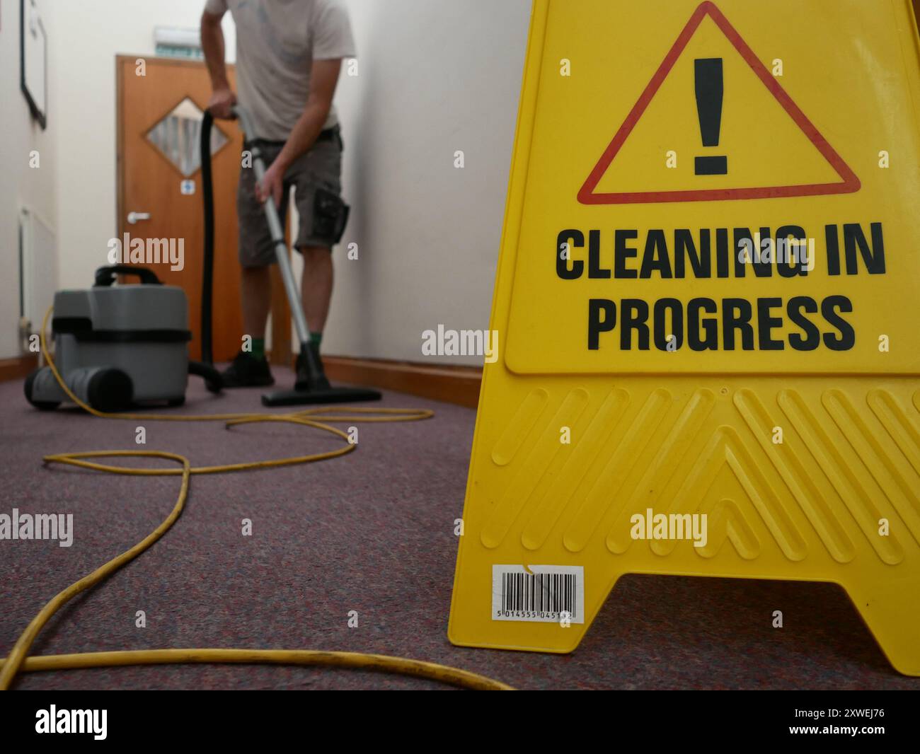 Cleaner at work vacuuming office corridor using a cleaning in progress sign. Stock Photo