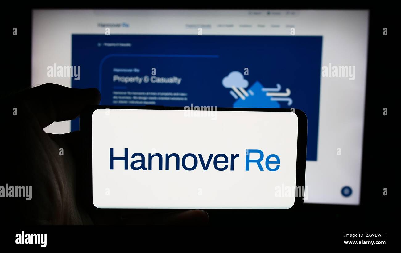 Person holding cellphone with logo of German reinsurance company Hannover Rück SE in front of business webpage. Focus on phone display. Stock Photo