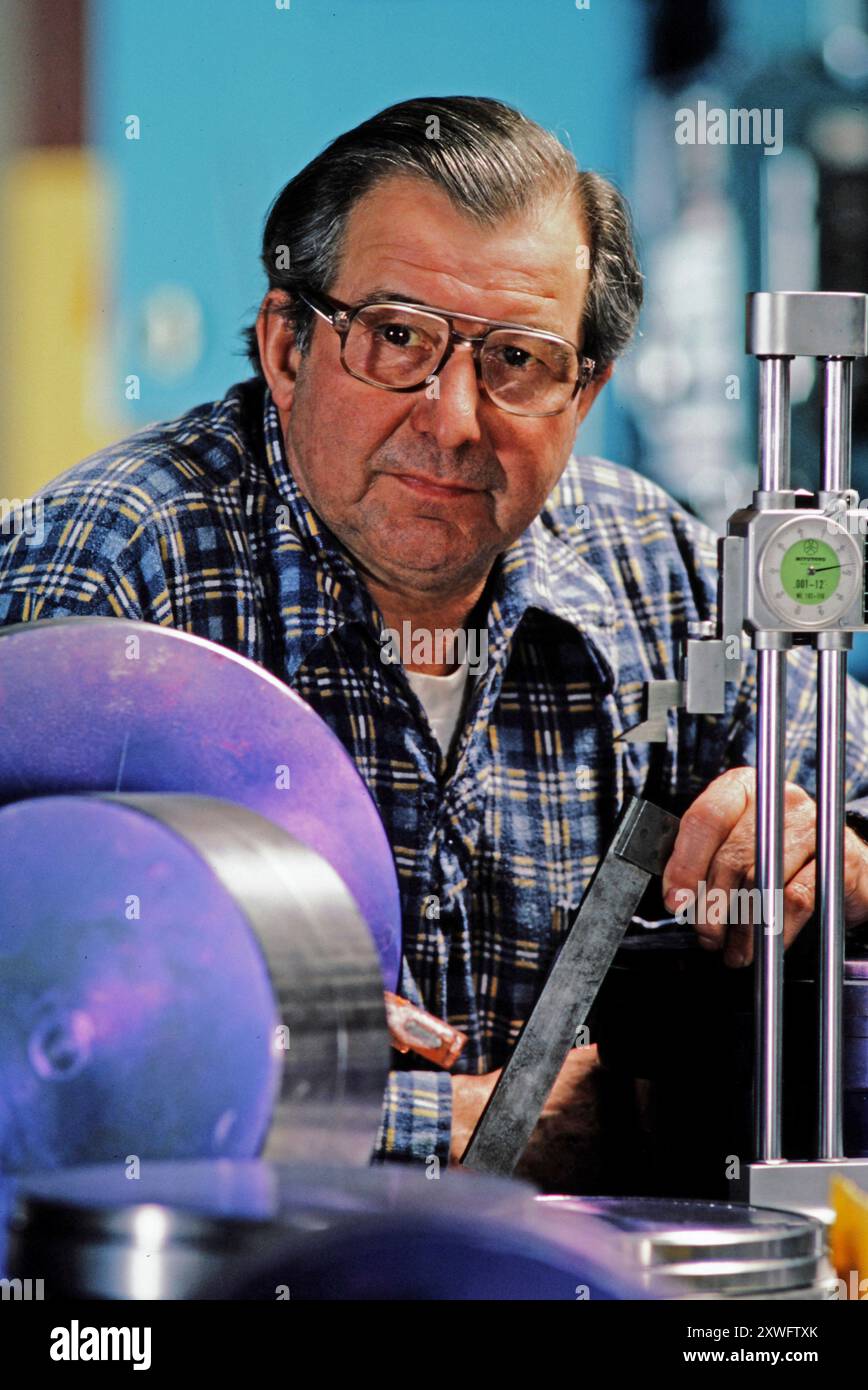 A skilled craftsman measures metal components in a workshop filled with tools and equipment. Stock Photo