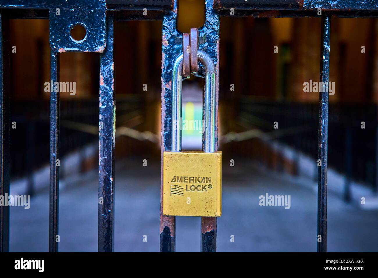 Close-Up Yellow Padlock on Rusty Gate with Blurred Passageway Background Stock Photo