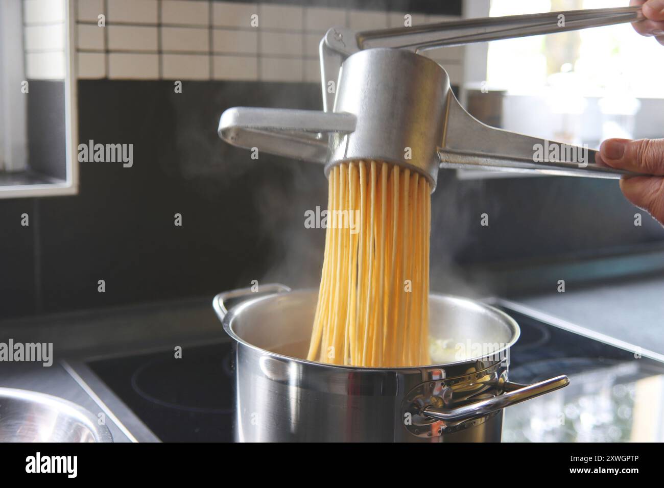 Spaetzle dough is pressed through a spaetzle press Stock Photo