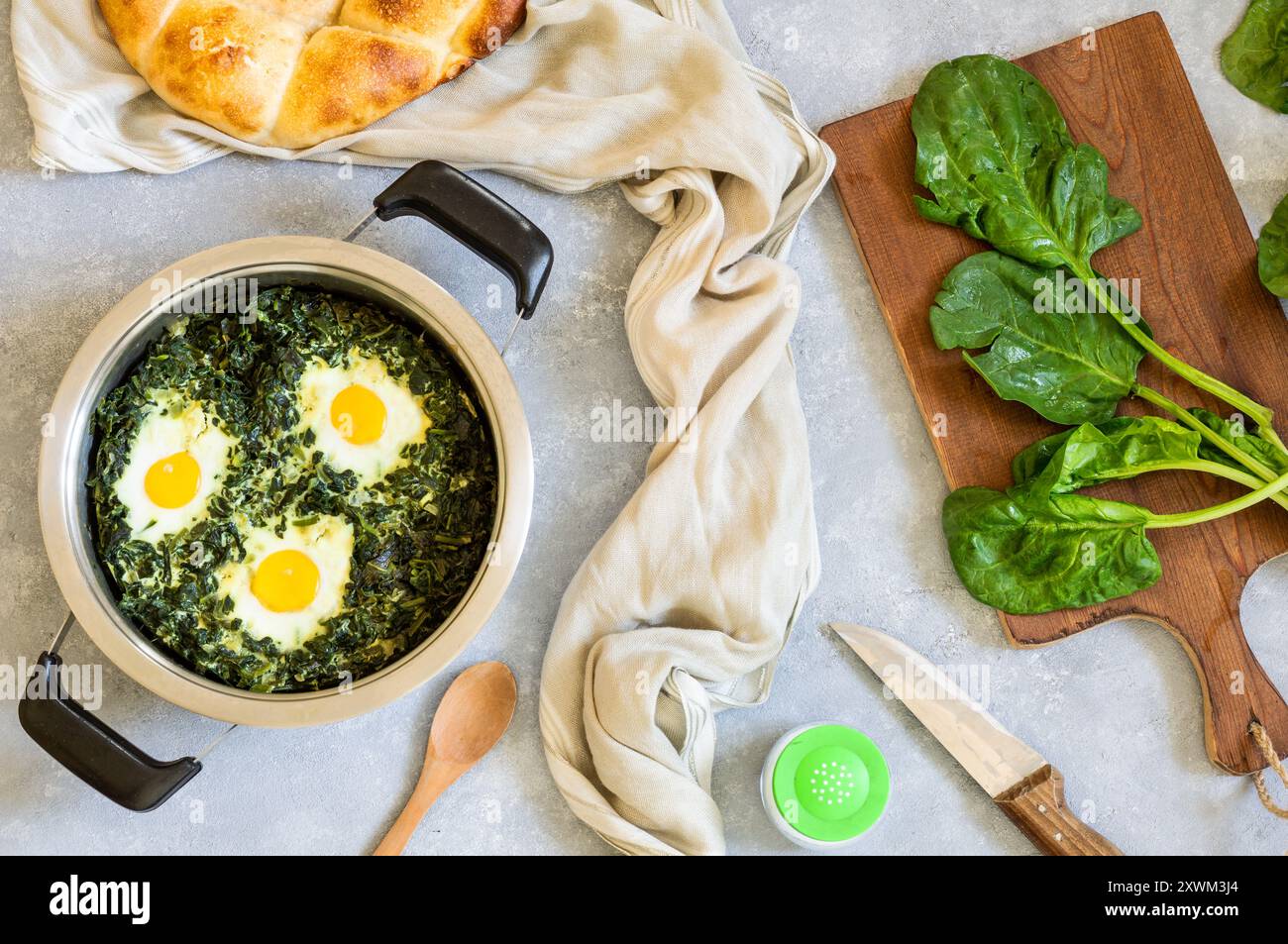 Roasted spinach and fried eggs in stewpot with fresh spinach vegetable on rustic table Stock Photo