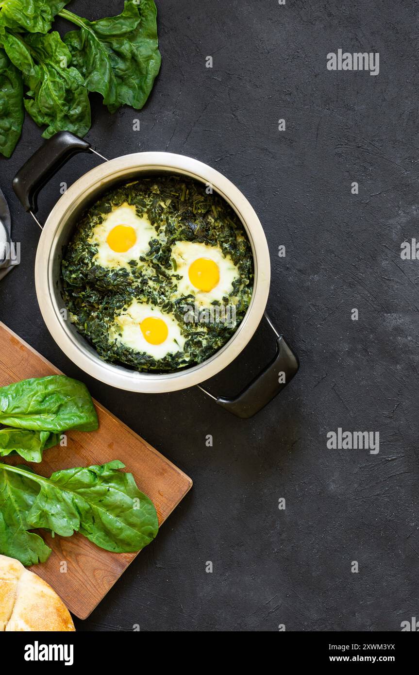 Roasted spinach and fried eggs in stewpot with fresh spinach vegetable on rustic table Stock Photo