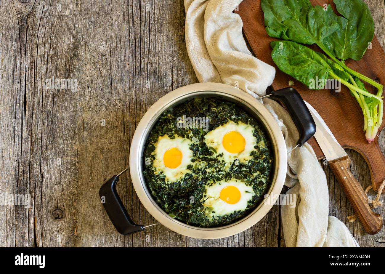 Roasted spinach and fried eggs in stewpot with fresh spinach vegetable on rustic table Stock Photo