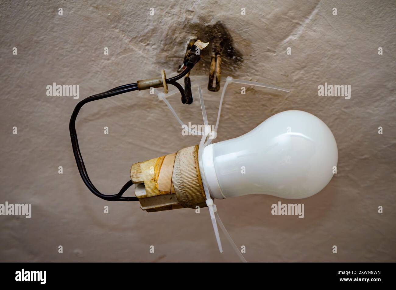 House problems, unsafe work concept. Photo of a lighting installation with an old ceramic light bulb socket improvised electrical wire connection Stock Photo