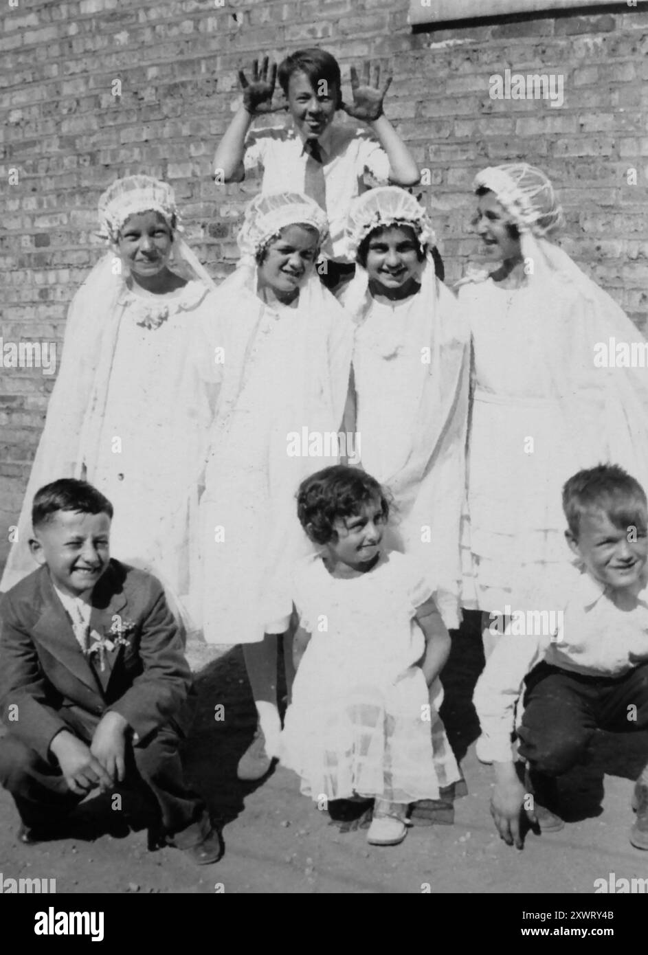 A young boy makes a face over his female cousins at their first communion, ca. 1935. Stock Photo