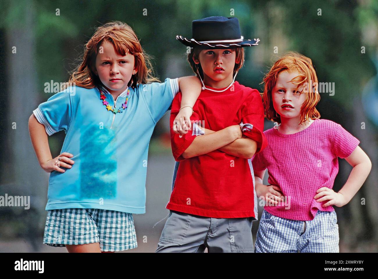 A portrait of three kids stand together with strong expressions, showcasing their casual summer attire while enjoying the outdoors. Stock Photo