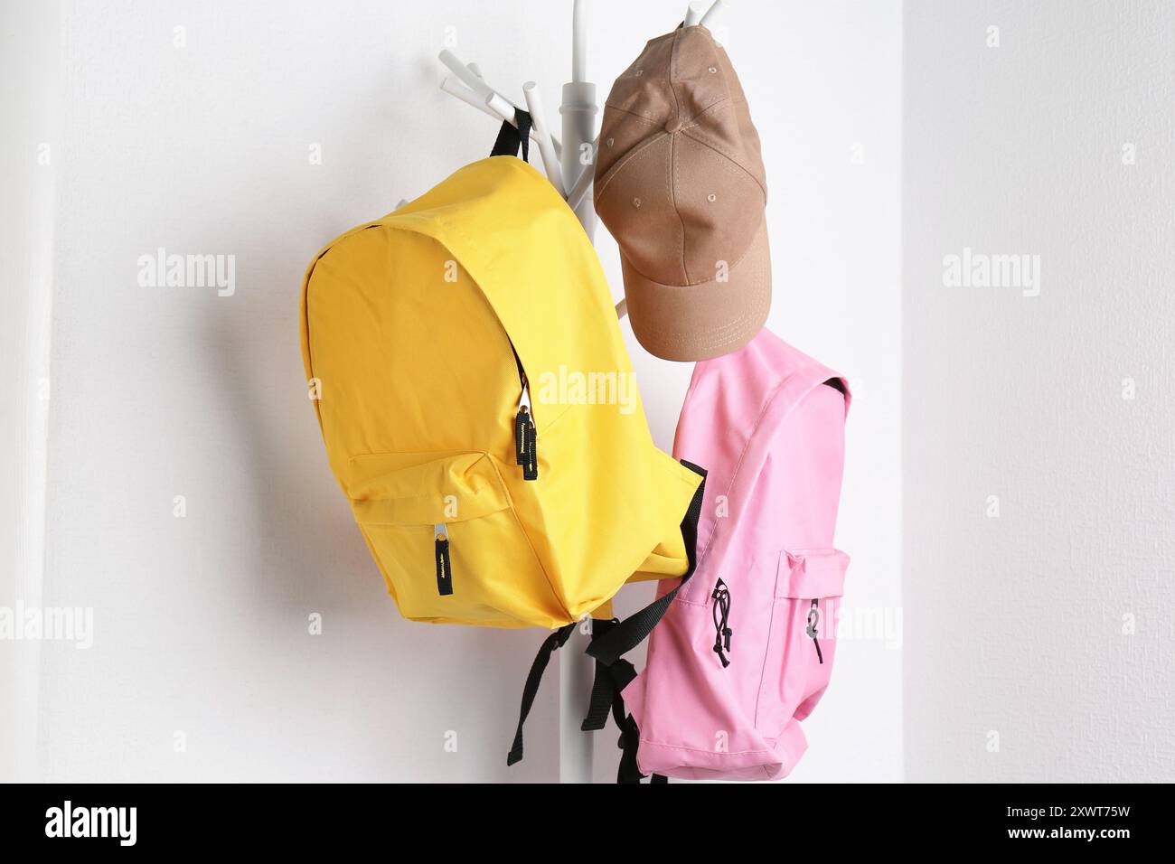 Bright backpacks and cap hanging on white wall Stock Photo