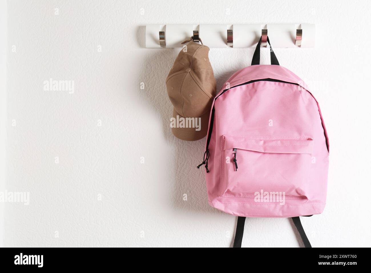 Pink backpack and cap hanging on white wall, space for text Stock Photo