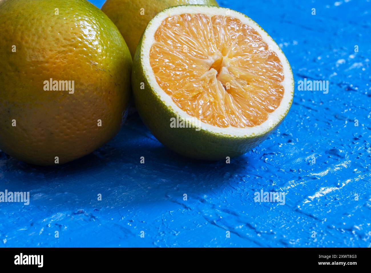 Half an orange with the pulp reflecting the light and resting on a whole orange. Stock Photo