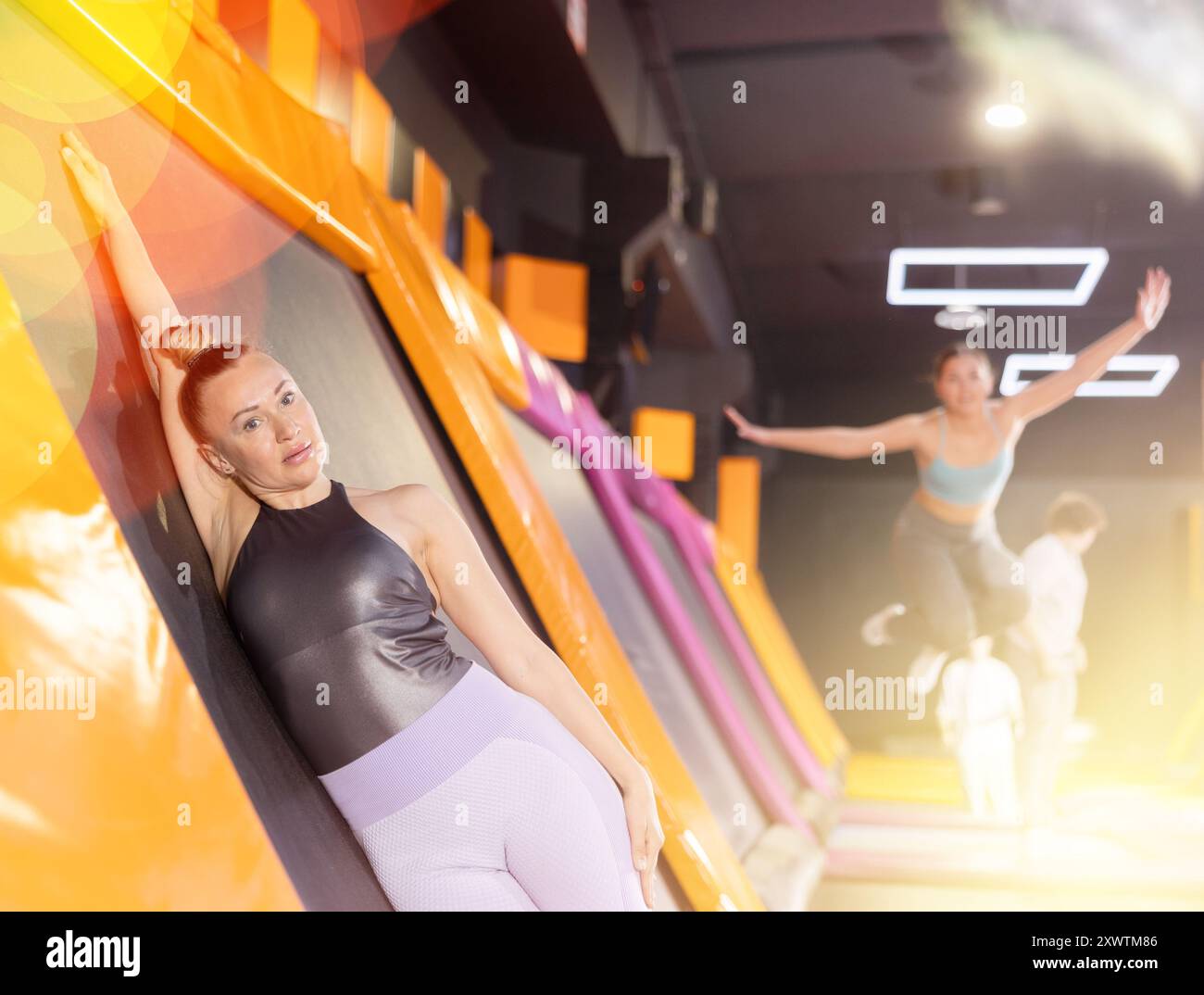 Middle-aged woman in sport clothes high jumping in trampoline arena ...