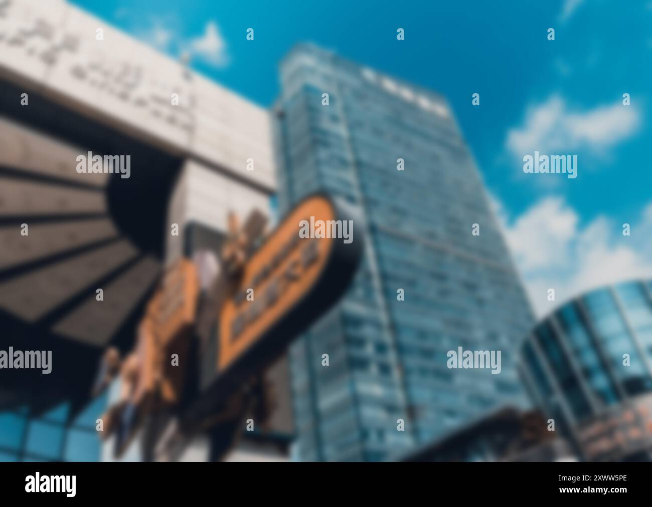 A blurred, abstract image of an urban environment in Shenzhen, China, featuring a tall glass building and a blue sky with bokeh background. Stock Photo